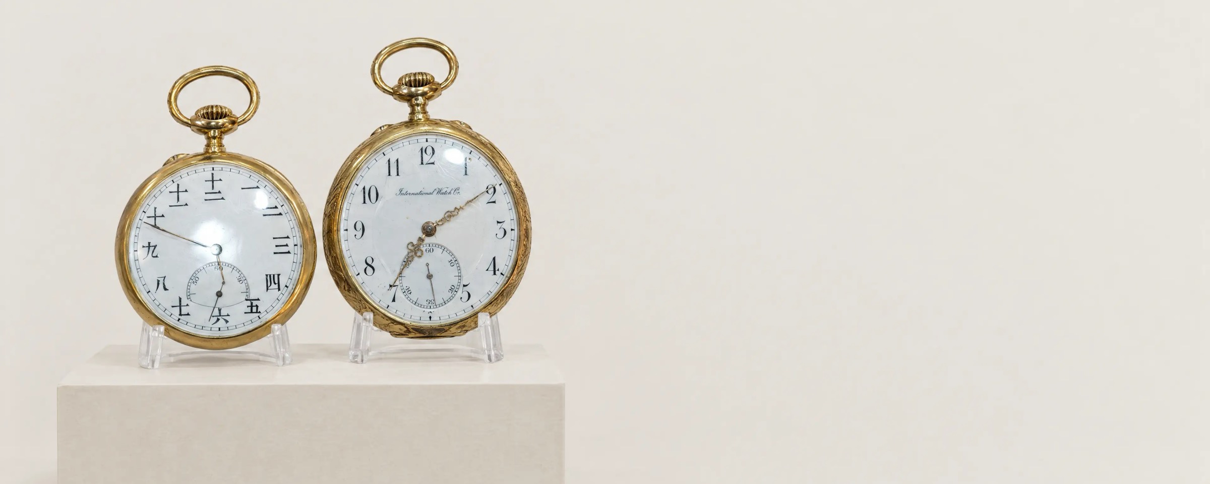 Two gold open-face pocket watches on stands, one with Japanese numerals