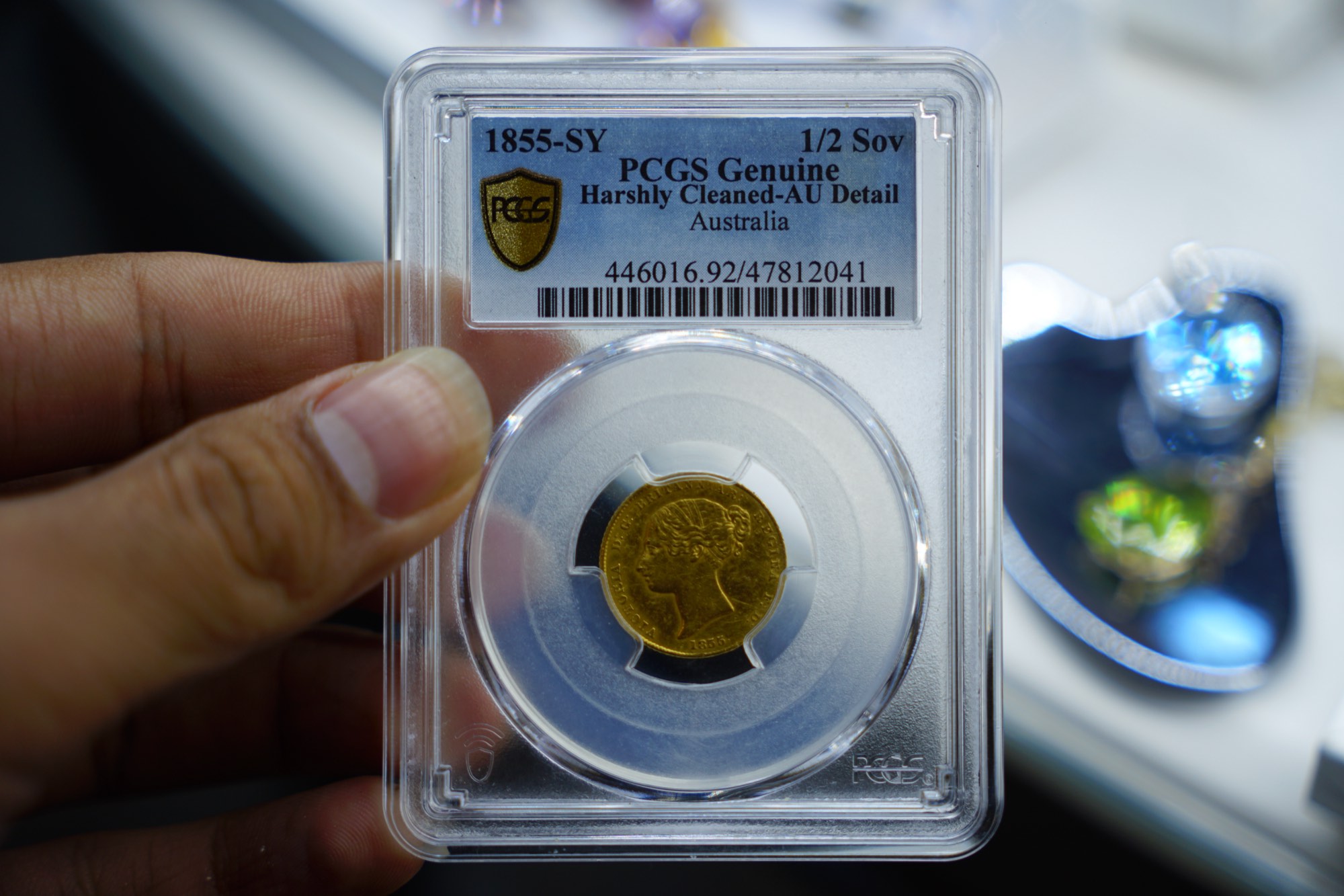 An 1855 Sydney Mint half sovereign, graded and encapsulated, held to the light